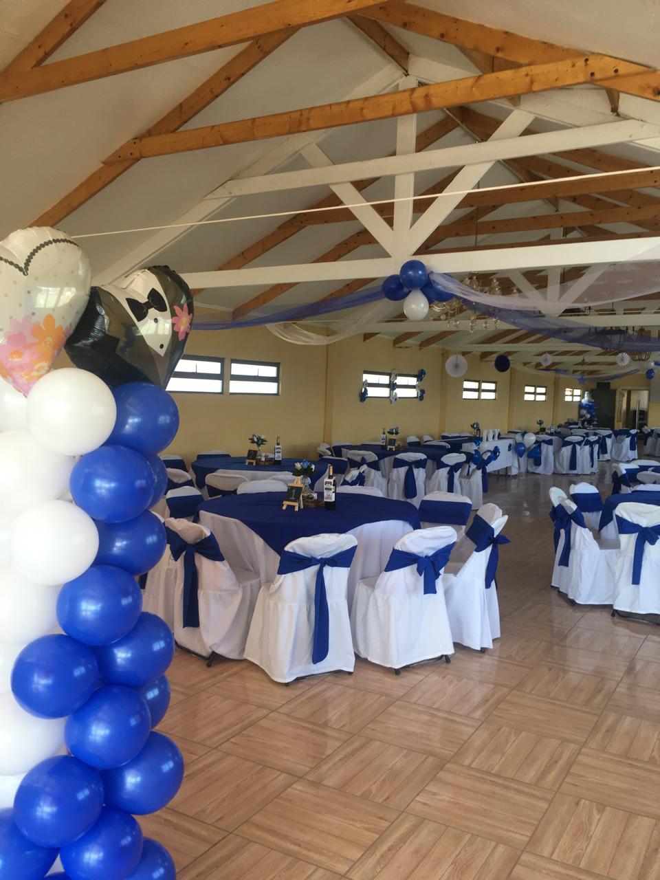 Salón de eventos decorado en blanco y azul, con arco de globos