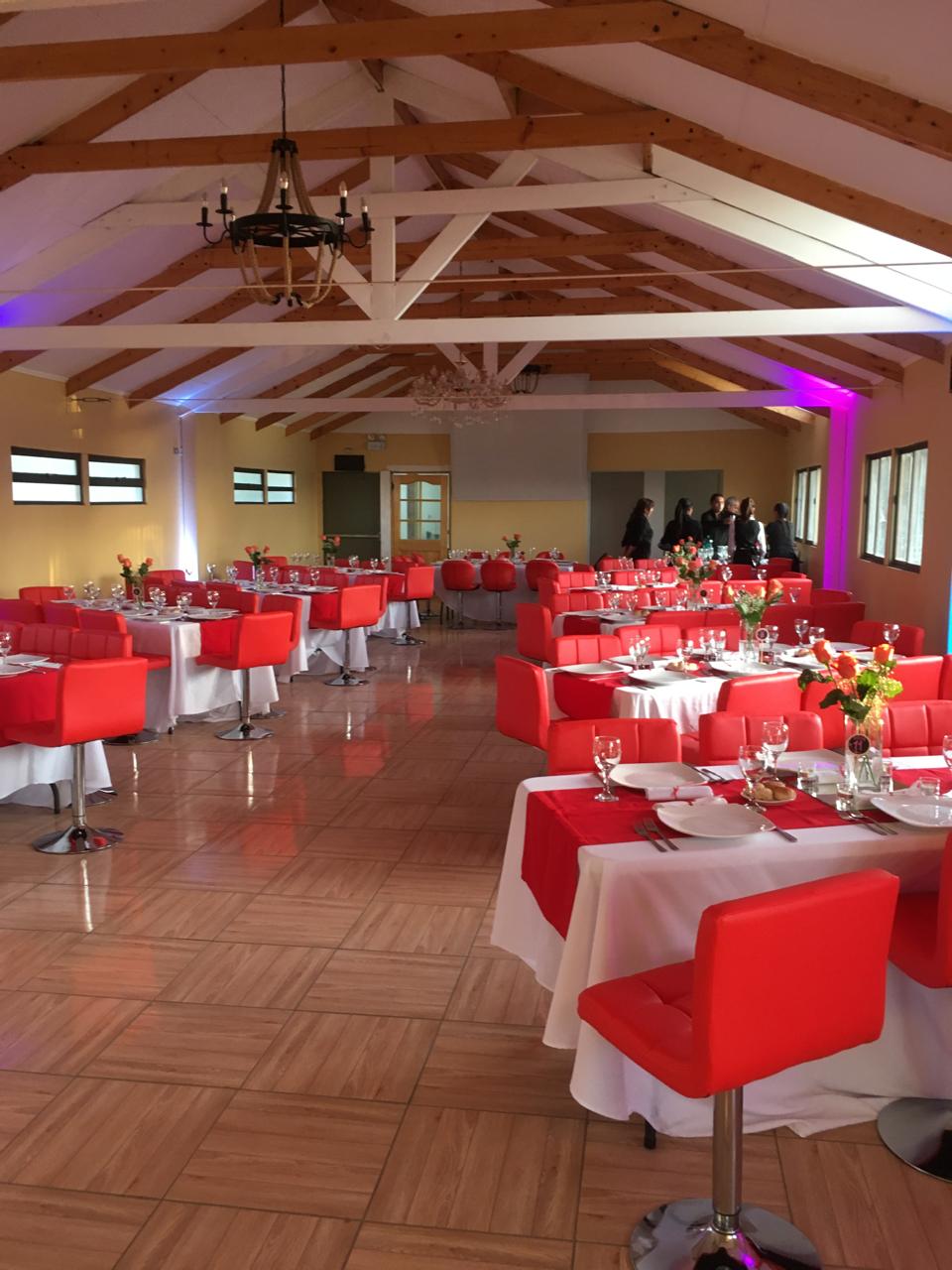Salón de eventos con mesas y sillas rojas, servicio de garzones